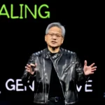Man in black leather jacket speaks on stage, gesturing, with "SCALING" and "GEN" visible in green and white text behind him.