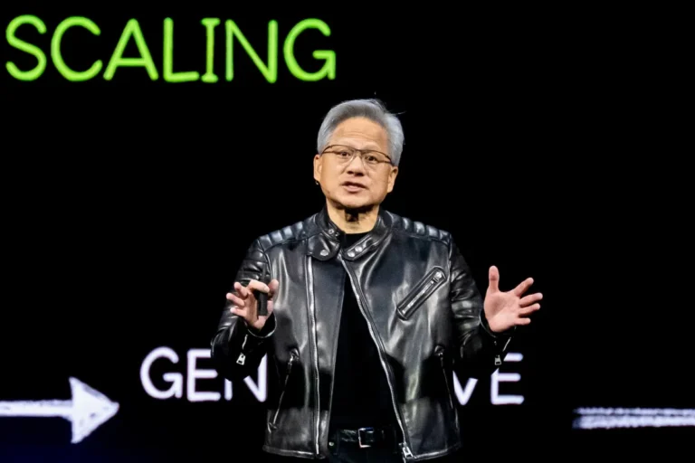 Man in black leather jacket speaks on stage, gesturing, with "SCALING" and "GEN" visible in green and white text behind him.