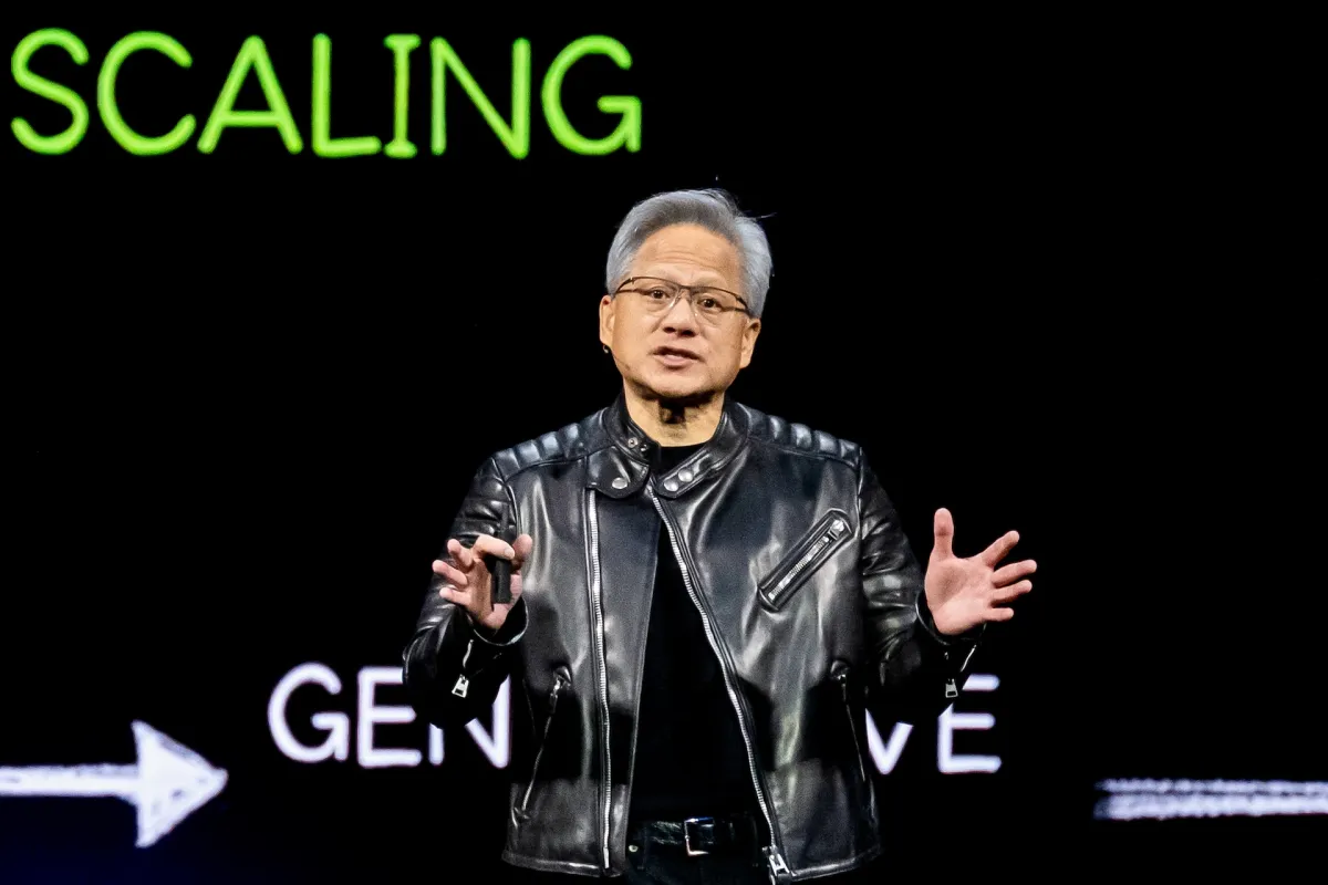 Man in black leather jacket speaks on stage, gesturing, with "SCALING" and "GEN" visible in green and white text behind him.