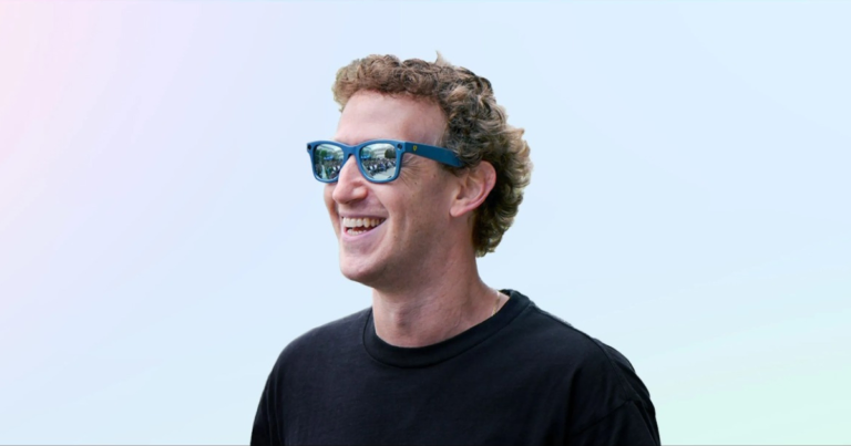 Smiling person wearing blue sunglasses and a black shirt against a light blue background.