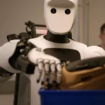 Humanoid robot with a white face and black eyes handling a basket, two people in the background observing.