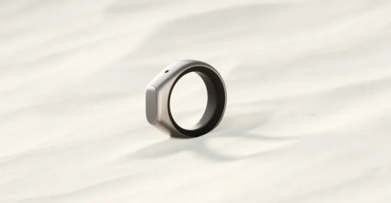 A sleek silver smart ring with a small button rests on a light, textured surface.