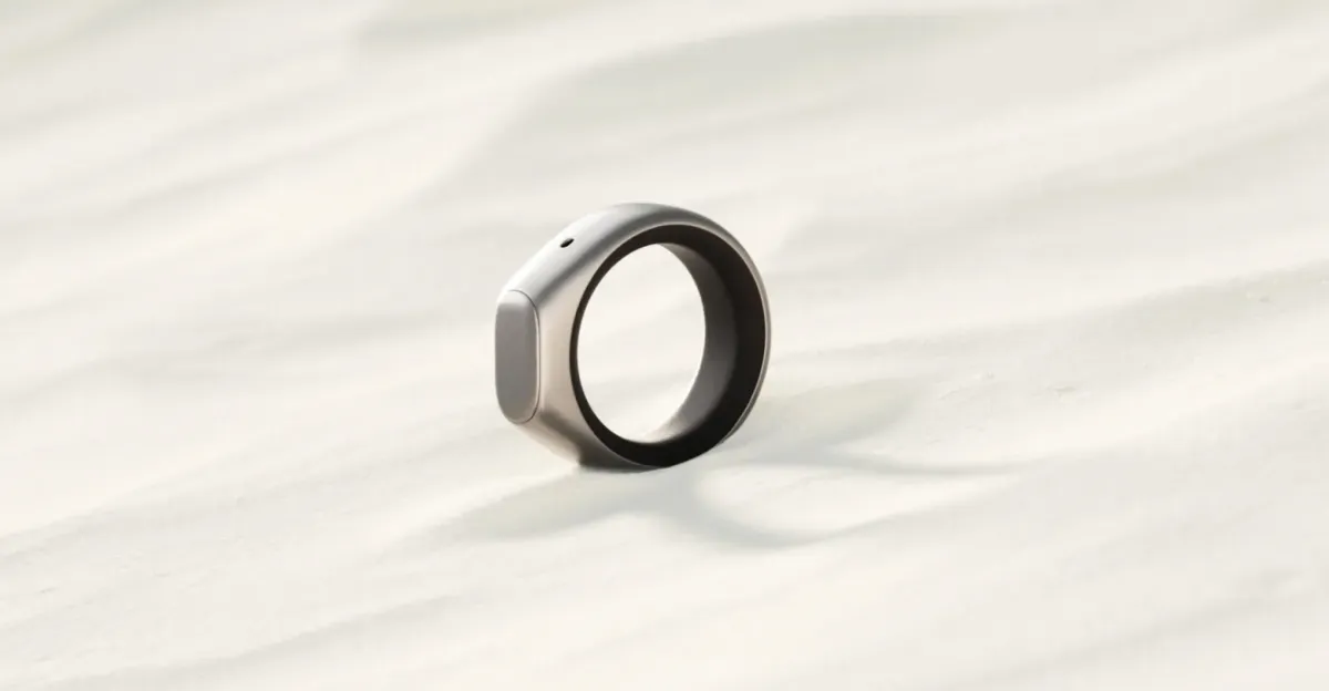 A sleek silver smart ring with a small button rests on a light, textured surface.