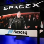 A large screen displays a man speaking with a group behind him, SpaceX logo above, Nasdaq sign below, digital clock shows...