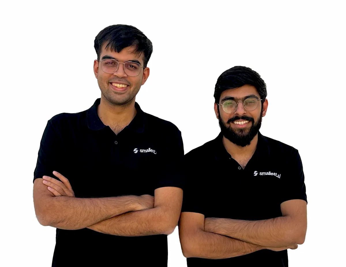 Two smiling men in black shirts with "smallest.ai" logos, standing with arms crossed against a white background.