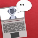 Laptop with a robot icon on screen and a speech bubble with ellipsis on a red background.