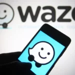Waze logo displayed on a smartphone screen in front of a larger Waze logo backdrop.