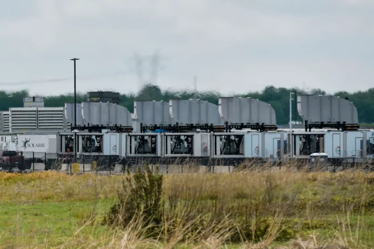 Row of gas turbines and equipment with "Solaris" logo in an industrial area, grassy field in the foreground, cloudy sky.