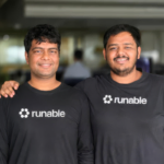 Two smiling individuals in black shirts with "runable" logo, standing in an office environment.