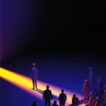 Silhouetted figures stand in a dark space facing a bright, vertical light beam.
