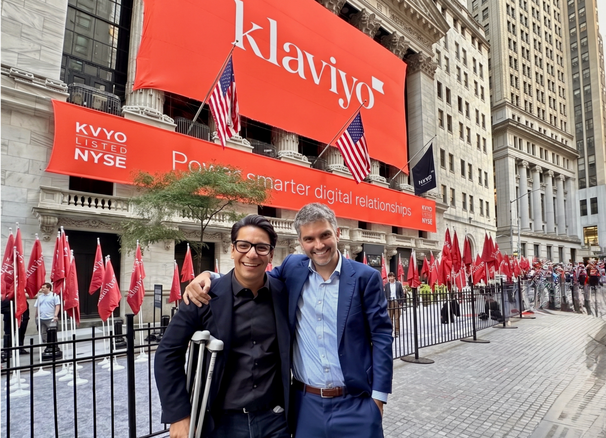 Two men smiling in front of the NYSE building with large Klaviyo banners and American flags.