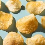 Several potato chips scattered on a light blue surface, casting soft shadows.