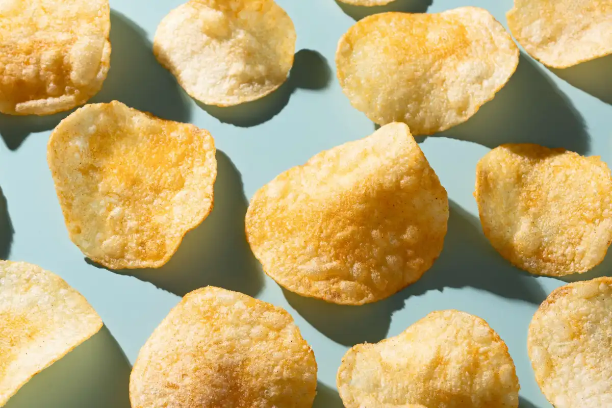 Several potato chips scattered on a light blue surface, casting soft shadows.