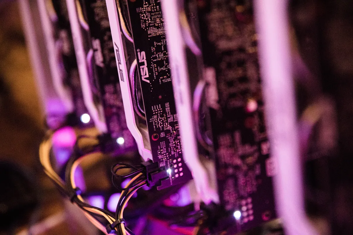 Rows of ASUS GPUs in a server rack with glowing indicator lights, connected by cables, illuminated by purple lighting