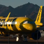 Yellow Spirit Airlines planes parked on tarmac with mountains in the background, fenced area in foreground.
