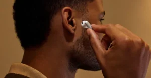 Person inserting a white earbud into their ear, close-up view, neutral background.