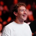 Smiling person in a white shirt, with a crowd blurred in the background.
