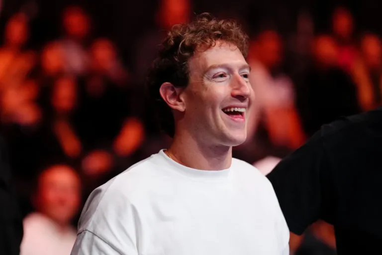 Smiling person in a white shirt, with a crowd blurred in the background.