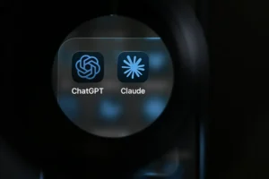 Close-up view of smartphone screen showing ChatGPT and Claude app icons under a magnifying lens, with a dark background.