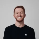 Smiling person with red hair wearing a black shirt against a plain background.