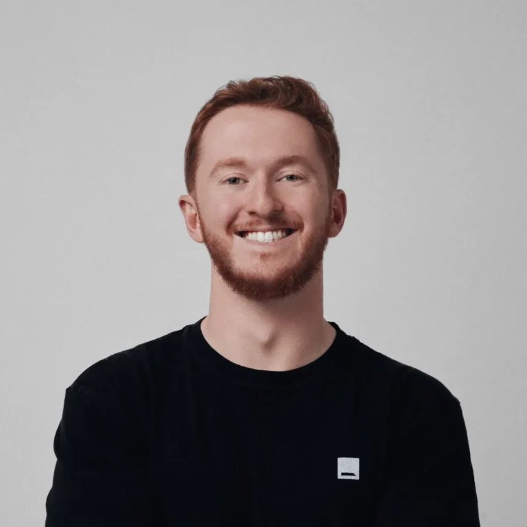 Smiling person with red hair wearing a black shirt against a plain background.