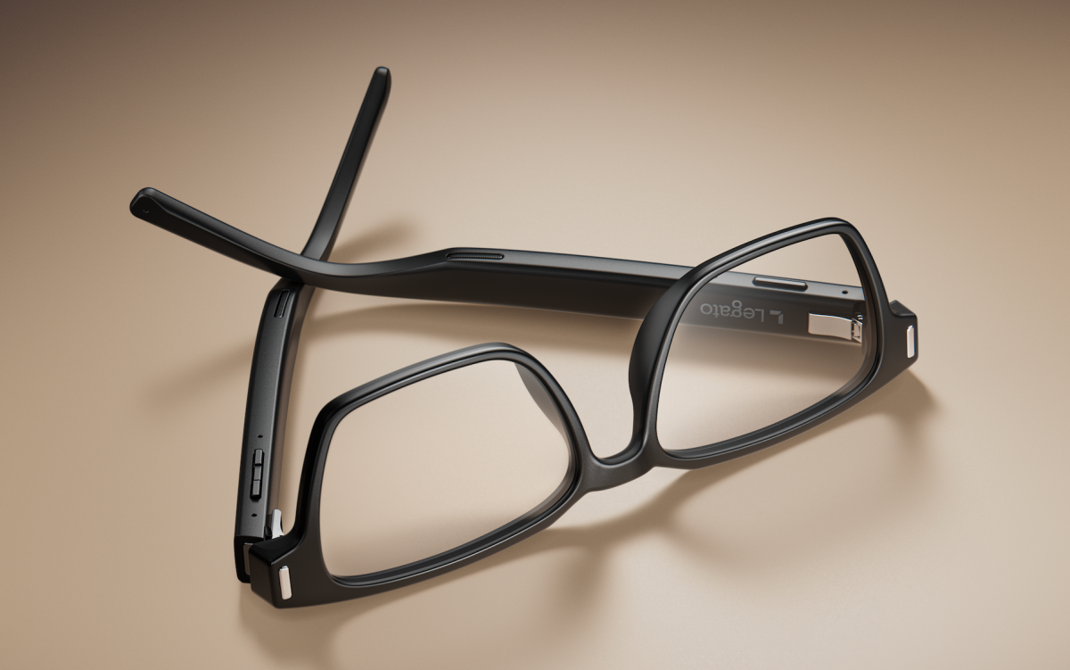 Black smart glasses with rectangular frames and integrated technology, resting on a beige surface.
