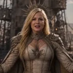 Woman in ornate armor and crown stands in front of a post-apocalyptic backdrop with towering structures and figures.