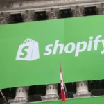 Large green Shopify banner displayed on a building with columns, featuring company logo and text, with American and Canadi...
