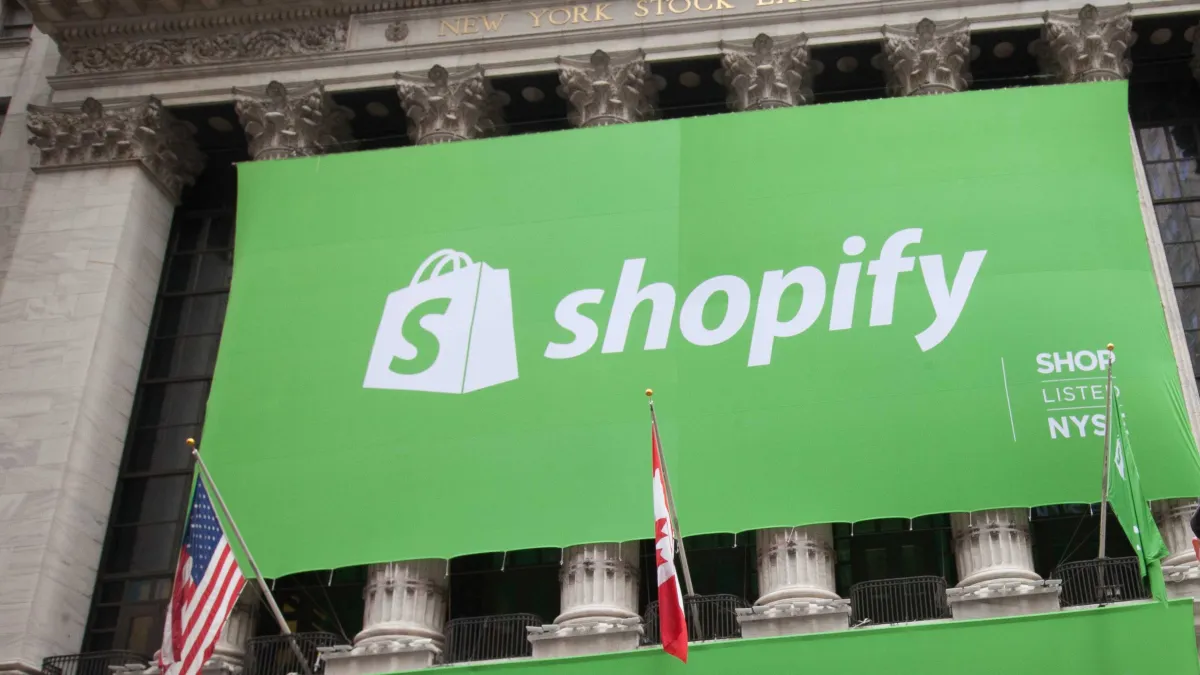 Large green Shopify banner displayed on a building with columns, featuring company logo and text, with American and Canadi...