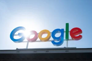 Google logo on a building, with sunlight shining through the letters against a clear blue sky.