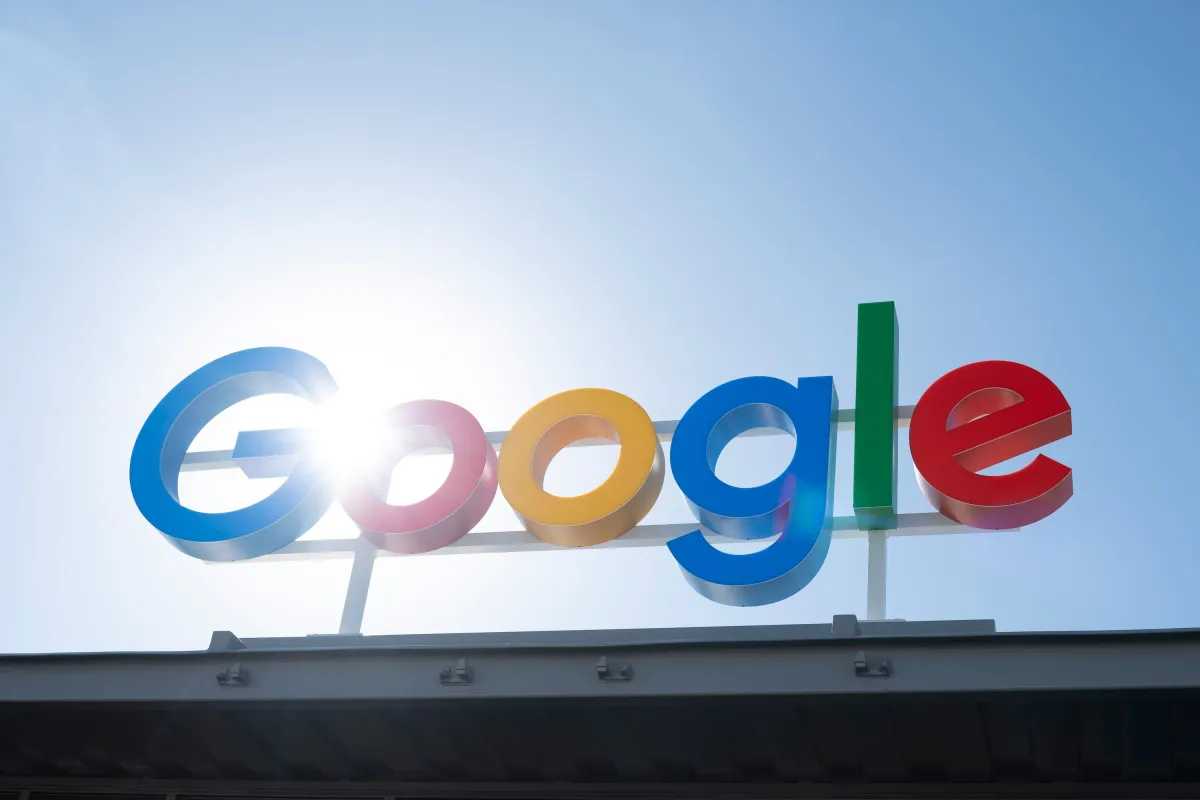 Google logo on a building, with sunlight shining through the letters against a clear blue sky.