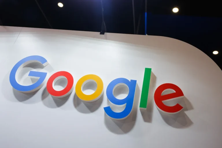Google logo in large colorful letters on a white wall, with spotlights in the background.