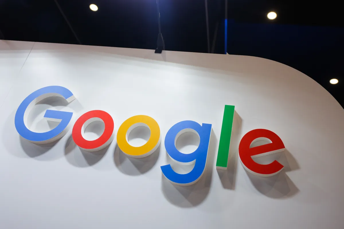 Google logo in large colorful letters on a white wall, with spotlights in the background.