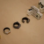 Three rings in different finishes and a white electronic device on a wooden surface.