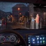 View from inside a car at night, dashboard showing 21:49, person waving by a parking meter, city street with lights and bu...
