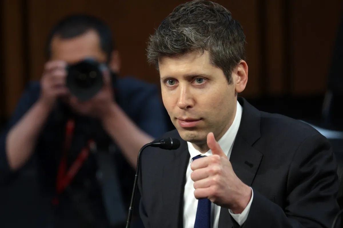 Man in a suit giving a thumbs-up at a microphone, with a photographer in the background capturing the moment.
