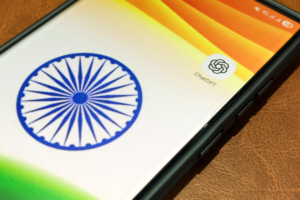 Smartphone screen displaying the ChatGPT app icon next to the Indian flag's Ashoka Chakra on a leather surface.