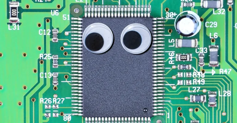 Microchip on a green circuit board with two googly eyes attached, surrounded by labeled electronic components.