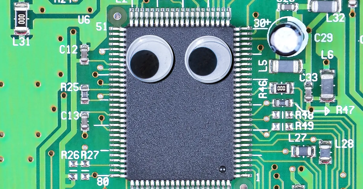 Microchip on a green circuit board with two googly eyes attached, surrounded by labeled electronic components.