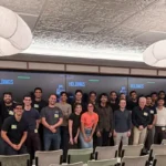 Large group of people smiling in a conference room with "Holdings" displayed on screens in the background.