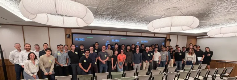 Large group of people smiling in a conference room with "Holdings" displayed on screens in the background.