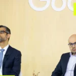 Two men in suits sit in front of a wooden wall with partial Google logo, yellow geometric overlay elements.