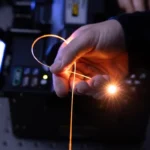 Hand holding glowing fiber optic cable looped, with equipment in the background.