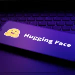 Hugging Face logo with smiley on a smartphone screen, placed on a laptop keyboard, purple lighting.