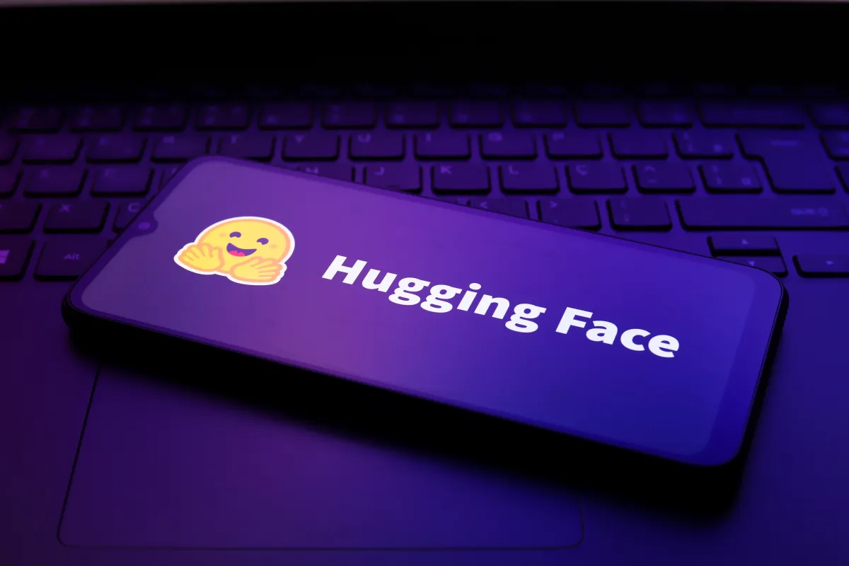 Hugging Face logo with smiley on a smartphone screen, placed on a laptop keyboard, purple lighting.
