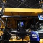 Yellow industrial vehicle with GPS and lidar technology displays at an exhibition.