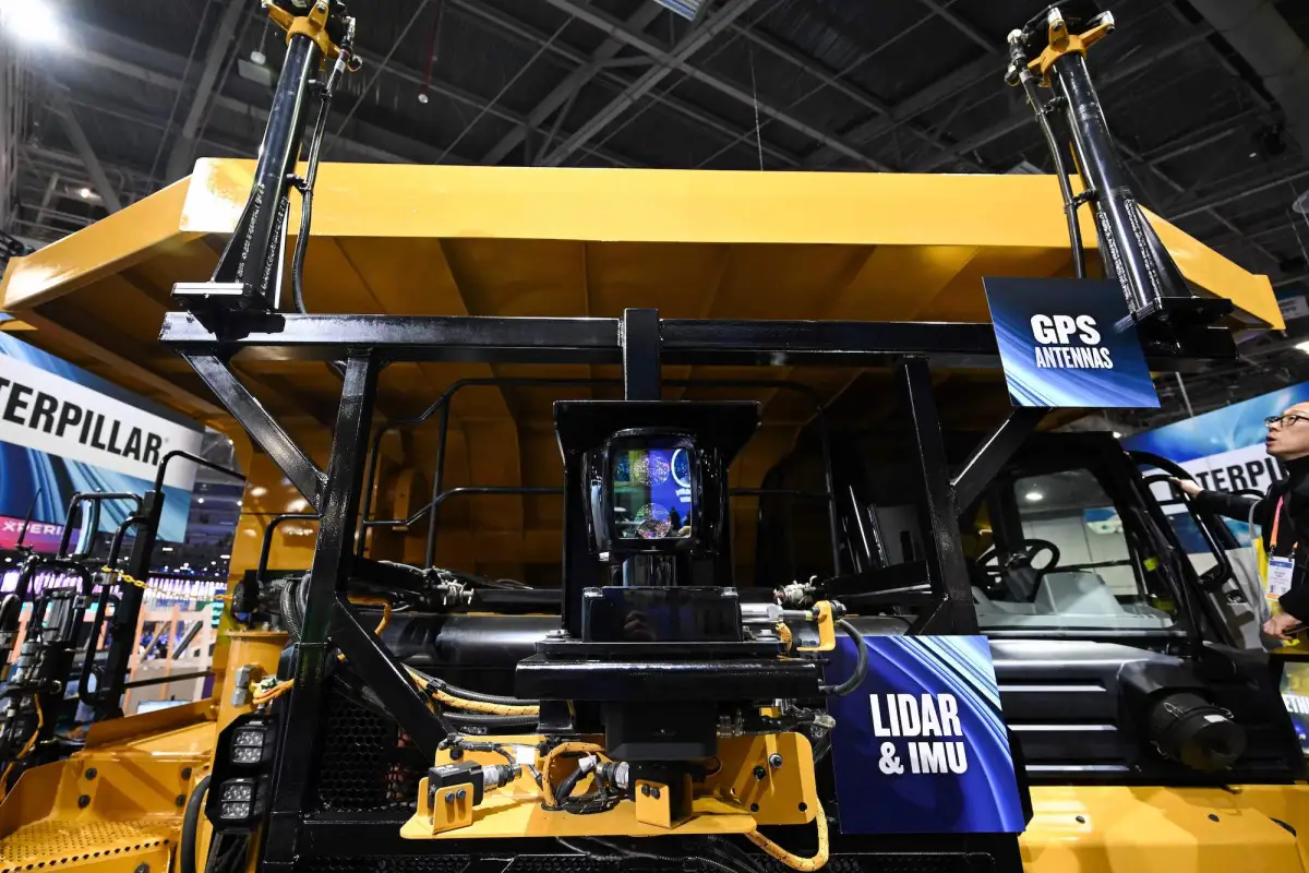 Yellow industrial vehicle with GPS and lidar technology displays at an exhibition.