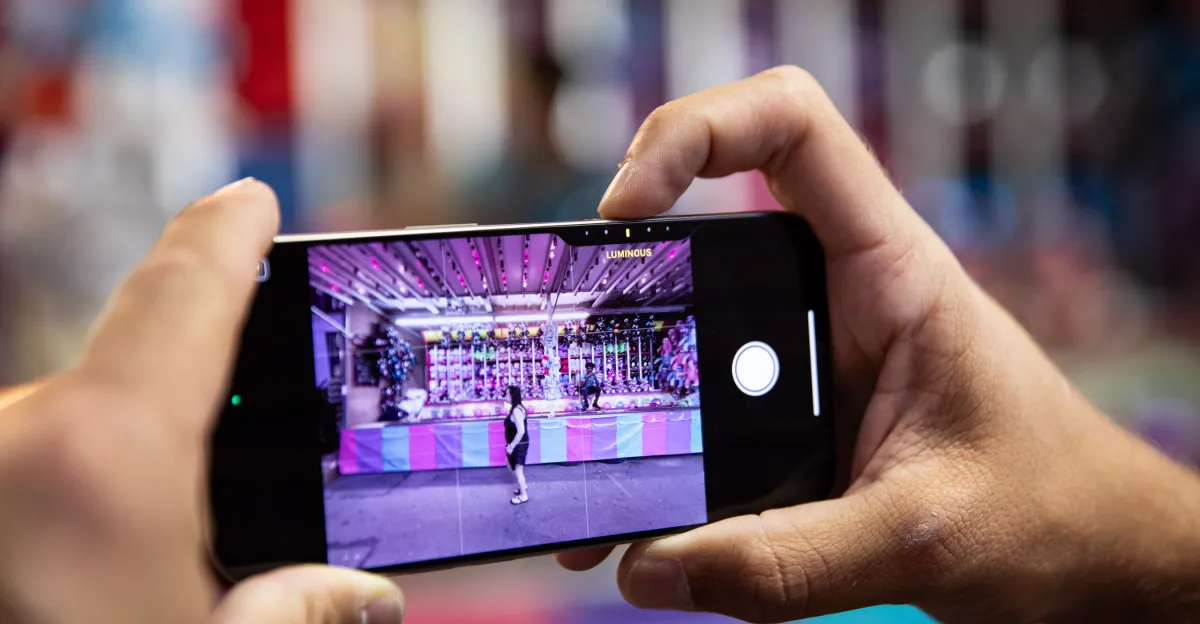 Hands holding a smartphone, capturing a photo of a colorful carnival game booth.