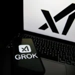 Smartphone displaying "GROK" and logo rests on a laptop keyboard, large logo on laptop screen.
