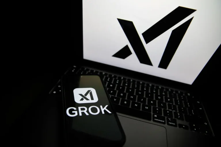 Smartphone displaying "GROK" and logo rests on a laptop keyboard, large logo on laptop screen.